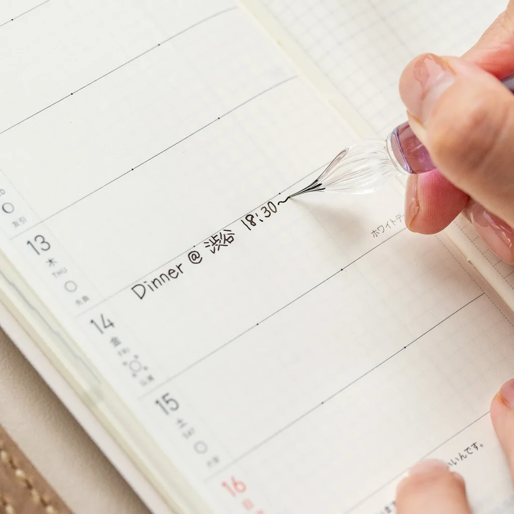 細字のガラスペンで手帳に書いている様子
